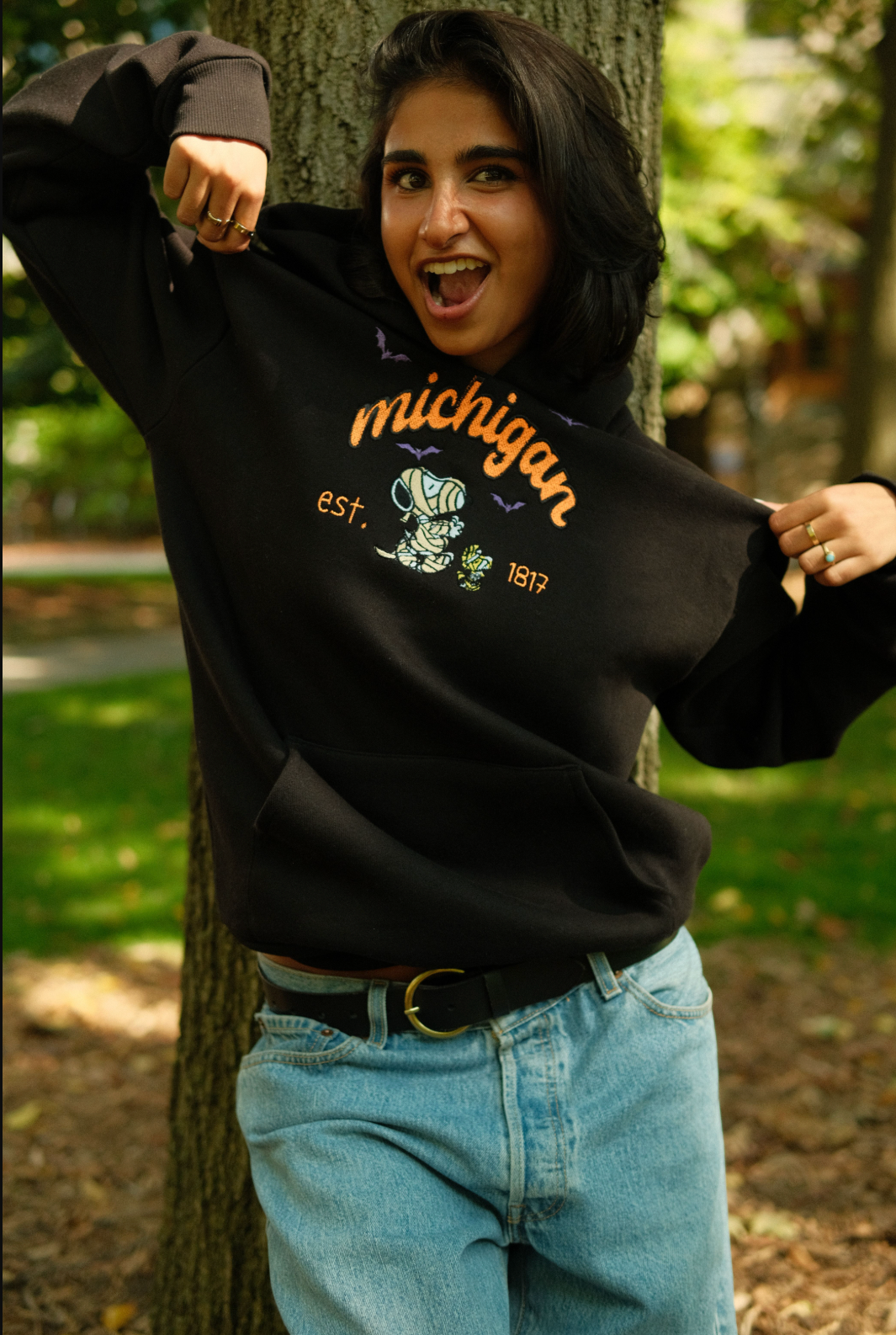 Person wearing a black 'Michigan' sweatshirt in a park setting SNOOPY and MITTN